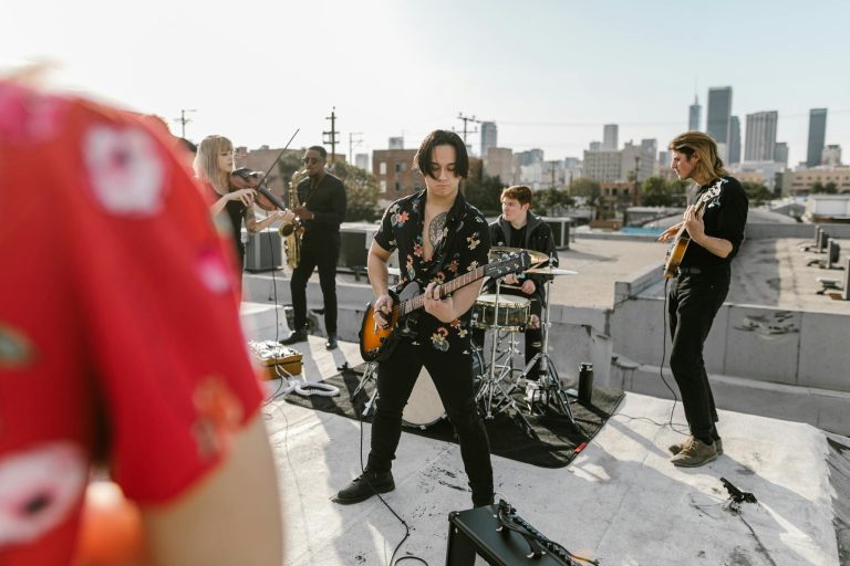 Musical band performing on a rooftop with instruments against a city skyline backdrop.
