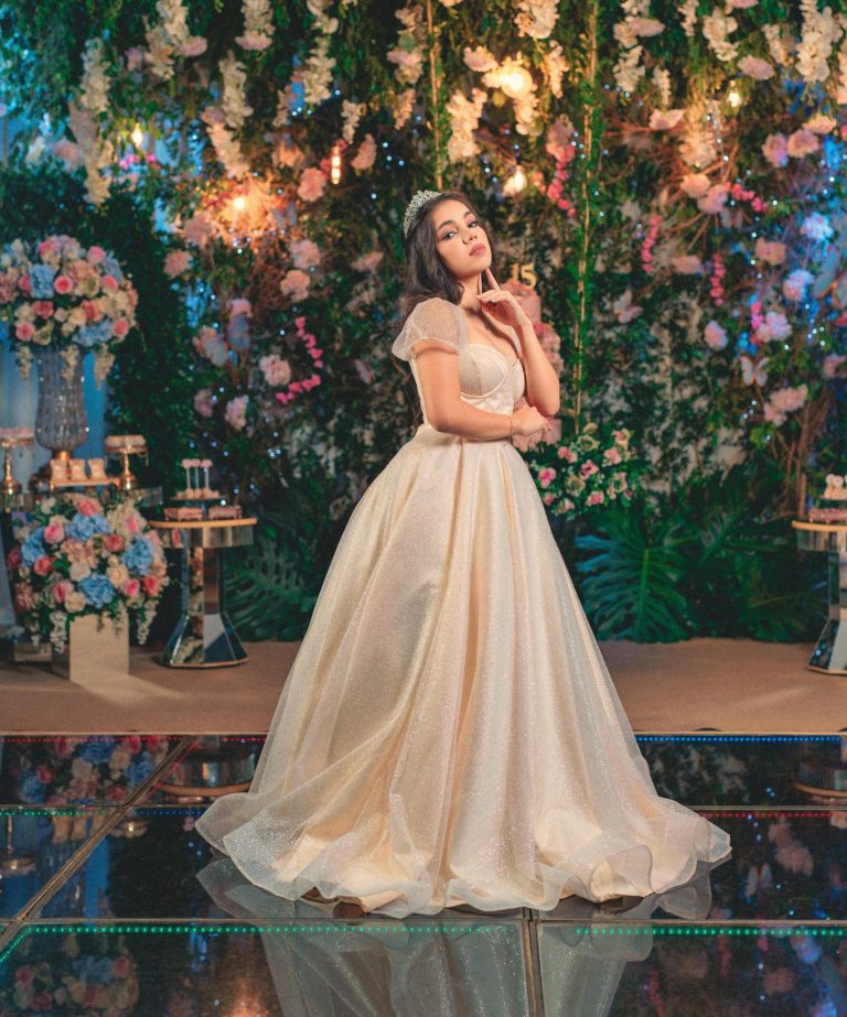 Beautiful quinceañera celebration featuring a teenage girl in a white dress surrounded by lavish floral decorations and chandeliers.