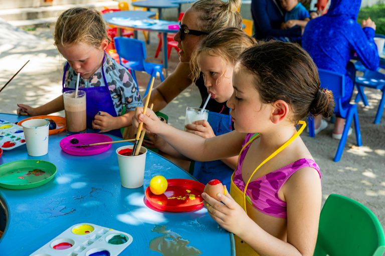 Children painting at an outdoor event while sipping refreshing beverages. Creative and joyful atmosphere.