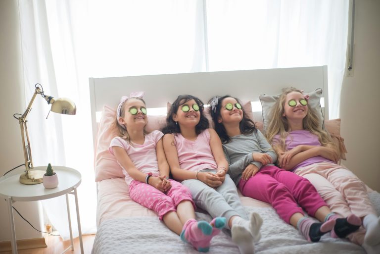 Four young girls having a fun spa day with cucumbers on eyes, lying in bed indoors.